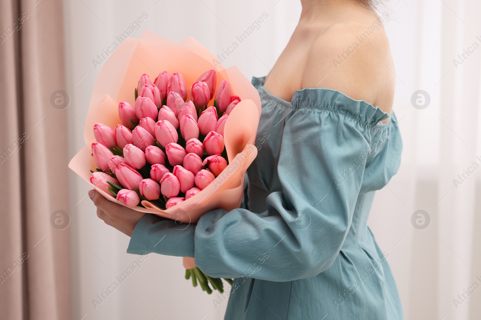 Photo of Woman holding bouquet of pink tulips indoors, closeup