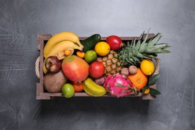 Different tropical fruits in wooden box on grey background, top view