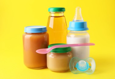 Photo of Healthy baby food, juice, milk, pacifier and spoon on yellow background