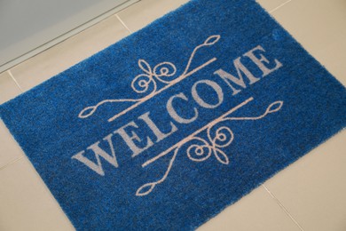 Photo of Beautiful blue doormat with word Welcome on floor near entrance, above view