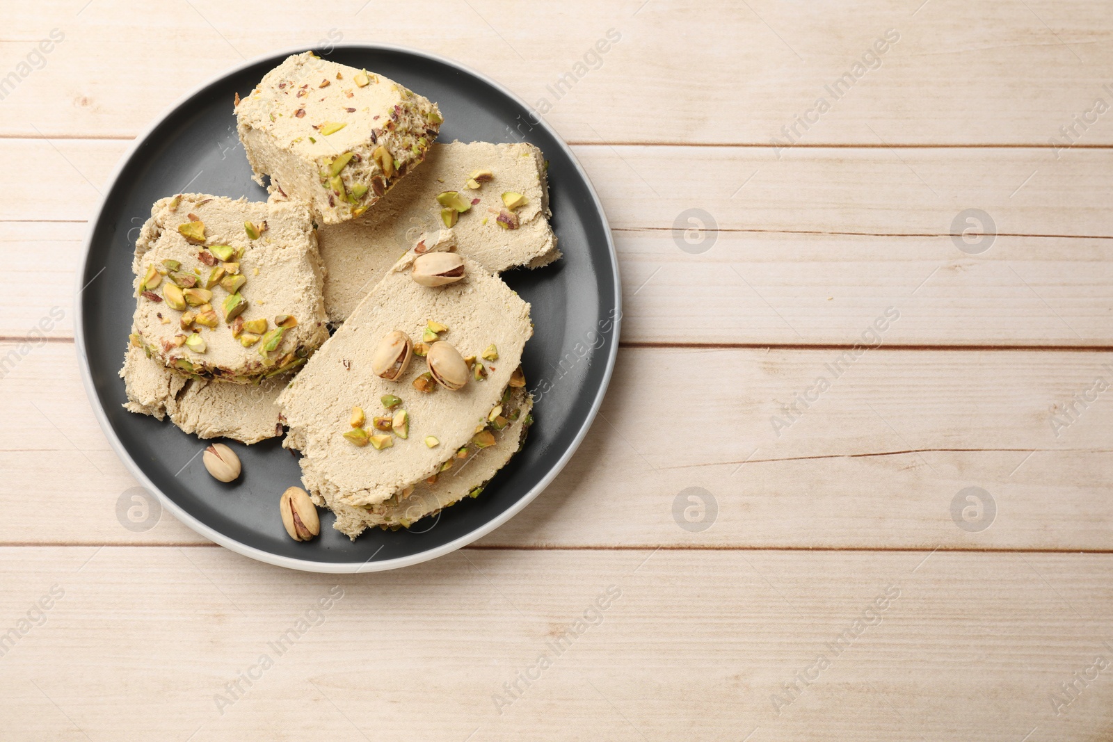 Photo of Pieces of tasty halva with pistachios on wooden table, top view. Space for text