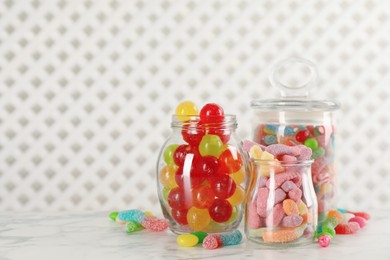 Jars with different delicious candies on white marble table, space for text