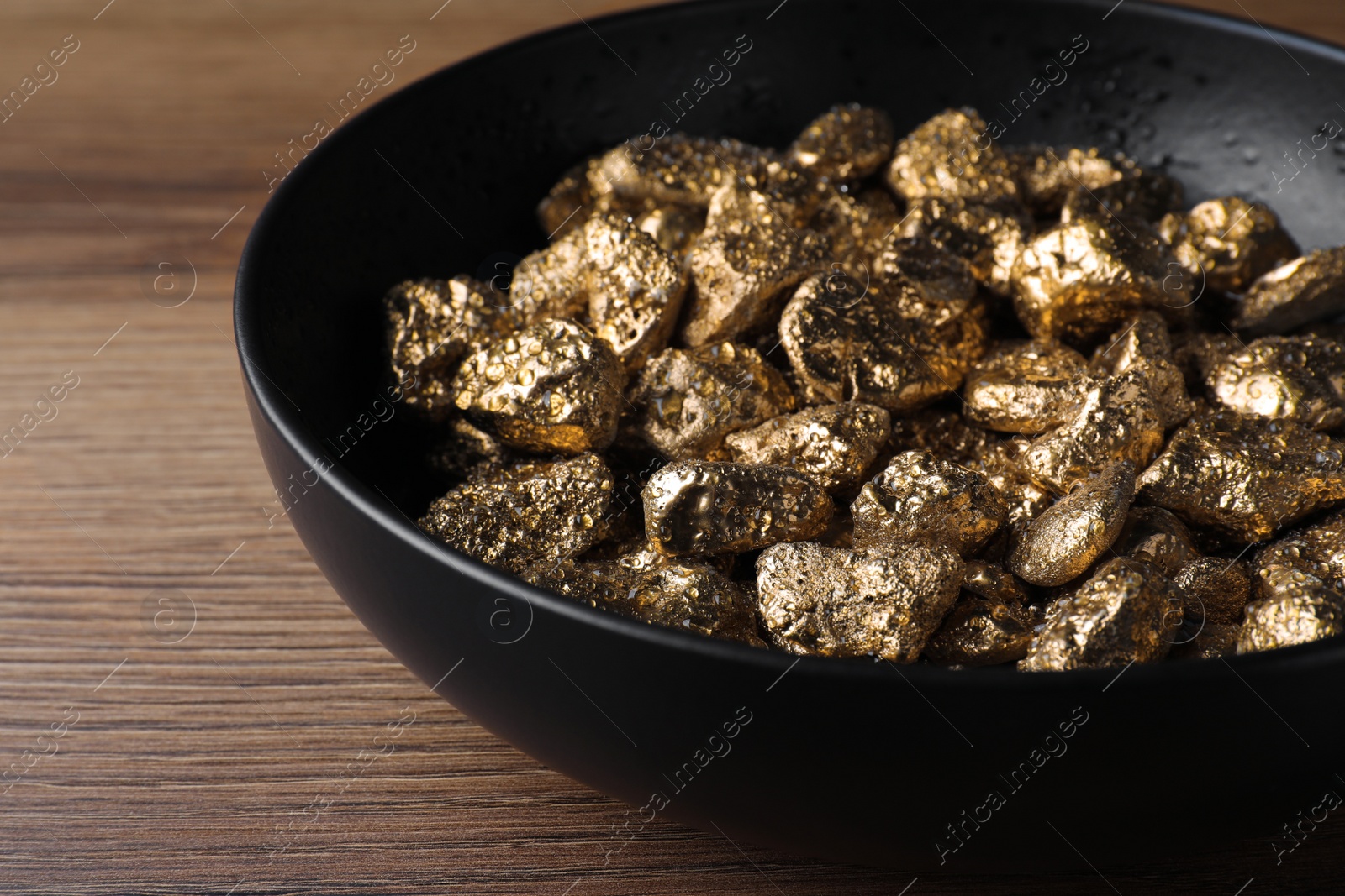 Photo of Bowl of gold nuggets on wooden table, closeup
