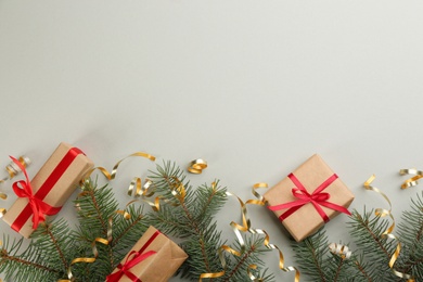 Photo of Shiny serpentine streamers, Christmas gifts and fir branches on light grey background, flat lay. Space for text