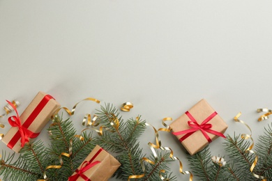 Shiny serpentine streamers, Christmas gifts and fir branches on light grey background, flat lay. Space for text