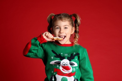 Photo of Cute little girl with Christmas gingerbread cookie on red background