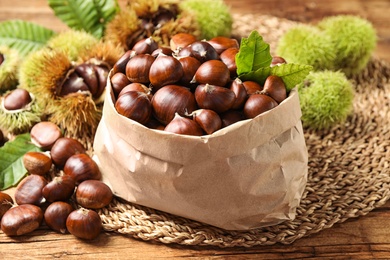 Fresh sweet edible chestnuts in paper bag on wooden table, closeup