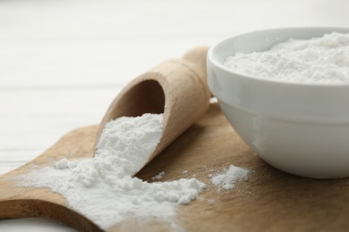 Baking powder in bowl and scoop on white wooden table, closeup