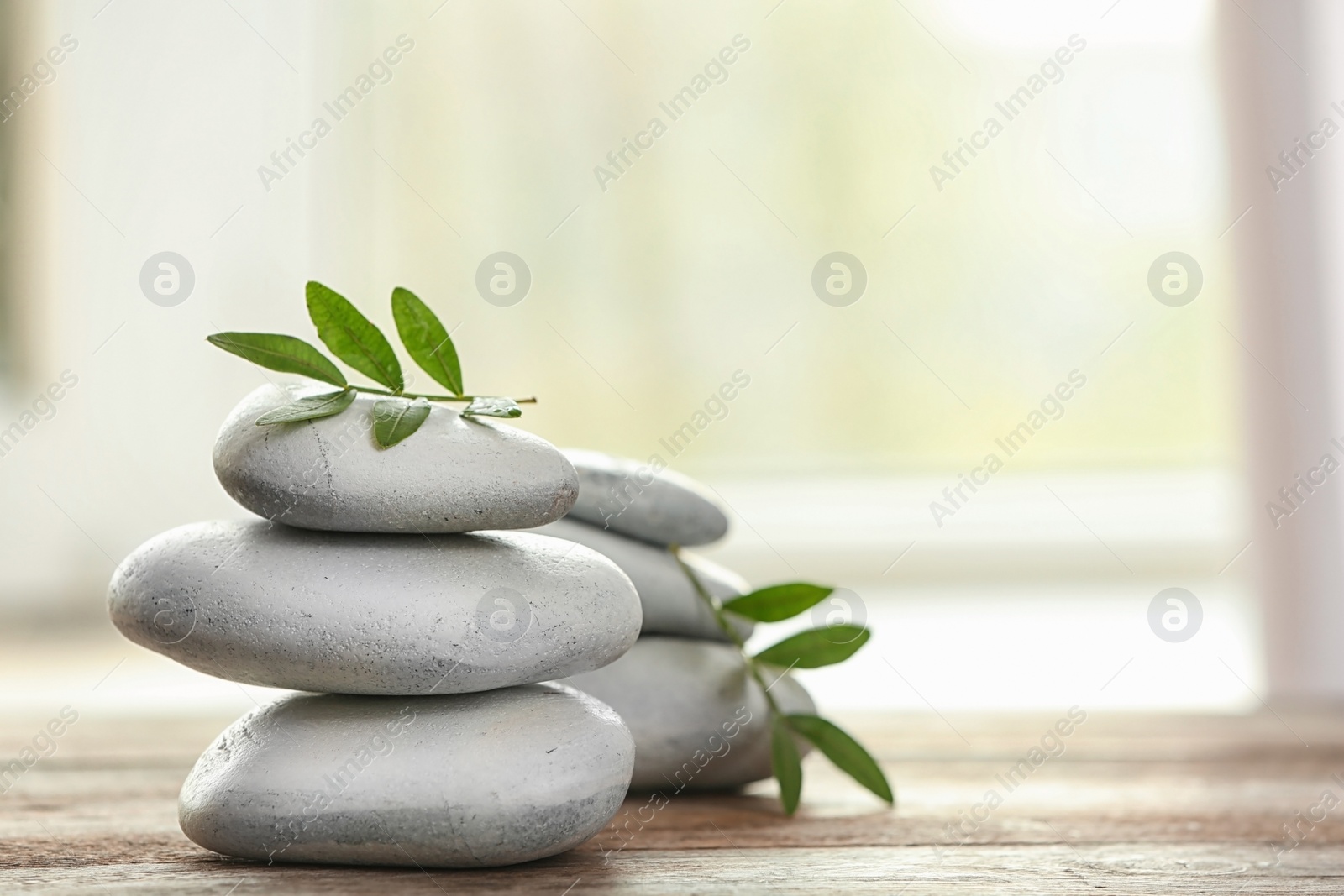 Photo of Spa stones and bamboo leaves on table against blurred background. Space for text