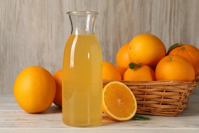 Many ripe oranges and fresh juice on light wooden table