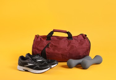 Photo of Sports bag and gym equipment on yellow background