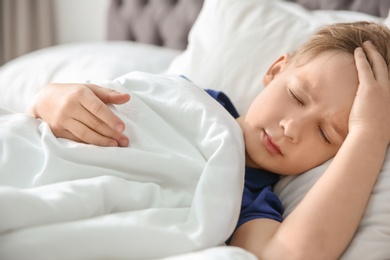 Little boy suffering from headache while lying in bed at home