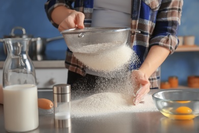 Woman sifting flour on table in kitchen