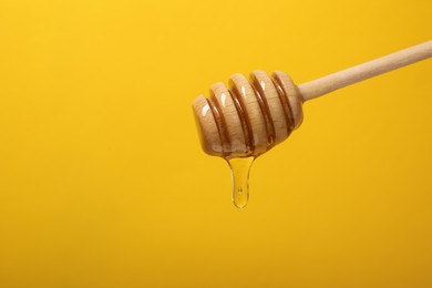 Photo of Pouring honey from dipper against yellow background, space for text