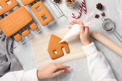 Photo of Top view of woman making gingerbread house at light grey marble table, closeup