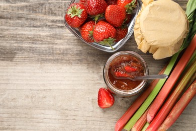 Photo of Tasty rhubarb jam, stems and strawberries on wooden table, flat lay. Space for text