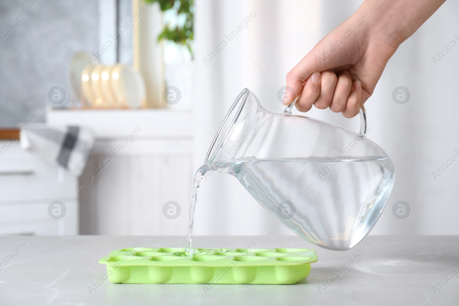 Photo of Woman pouring water into ice cube tray at grey marble table, closeup