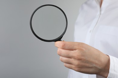 Woman holding magnifying glass on grey background, closeup. Find keywords concept