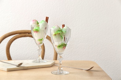 Glasses with snow ice cream dessert on table against light wall. Space for text