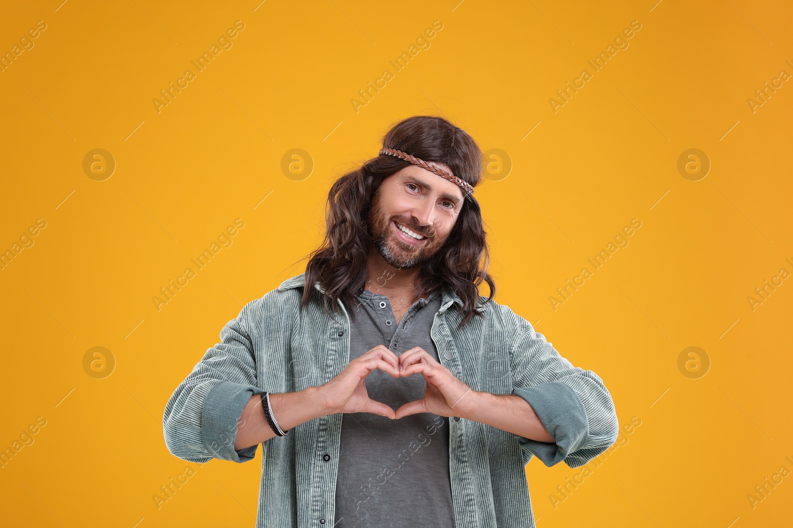 Photo of Stylish hippie man making heart with hands on orange background