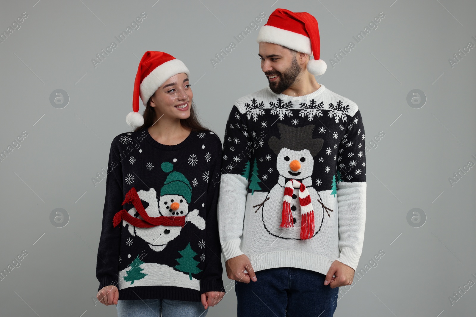 Photo of Young couple in Christmas sweaters and Santa hats on grey background