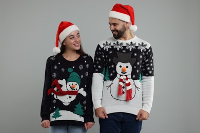 Photo of Young couple in Christmas sweaters and Santa hats on grey background