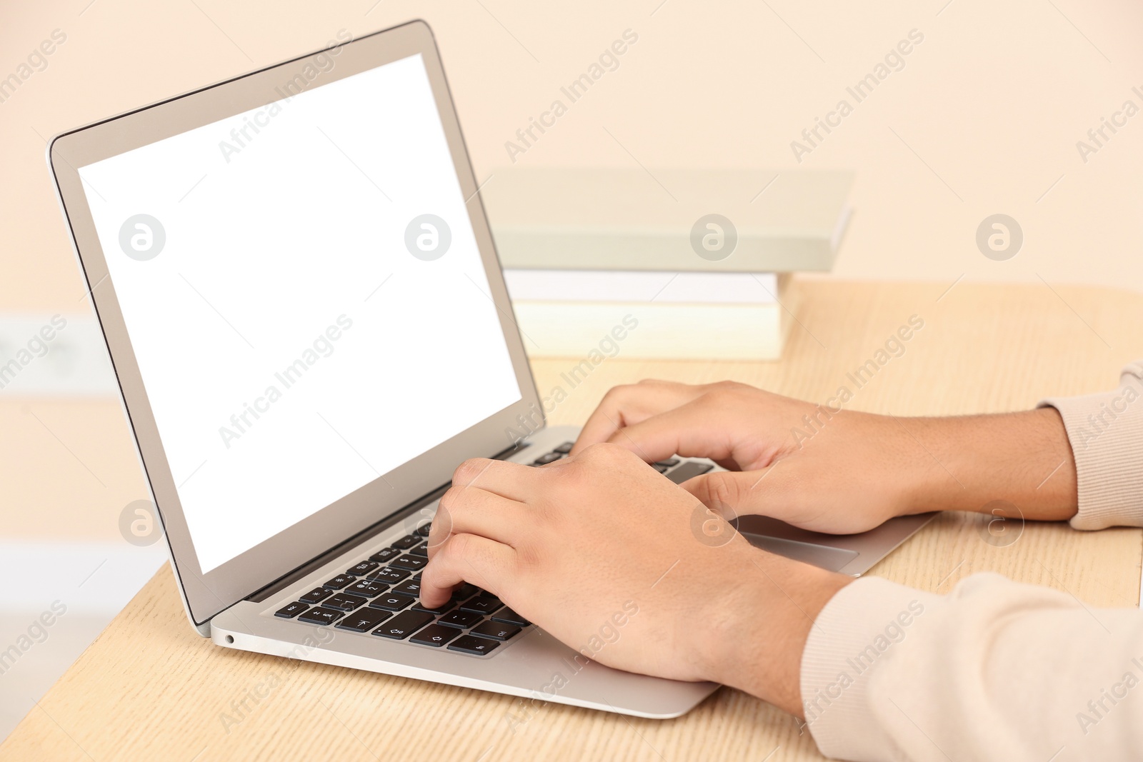 Photo of African American man typing on laptop at wooden table indoors, closeup