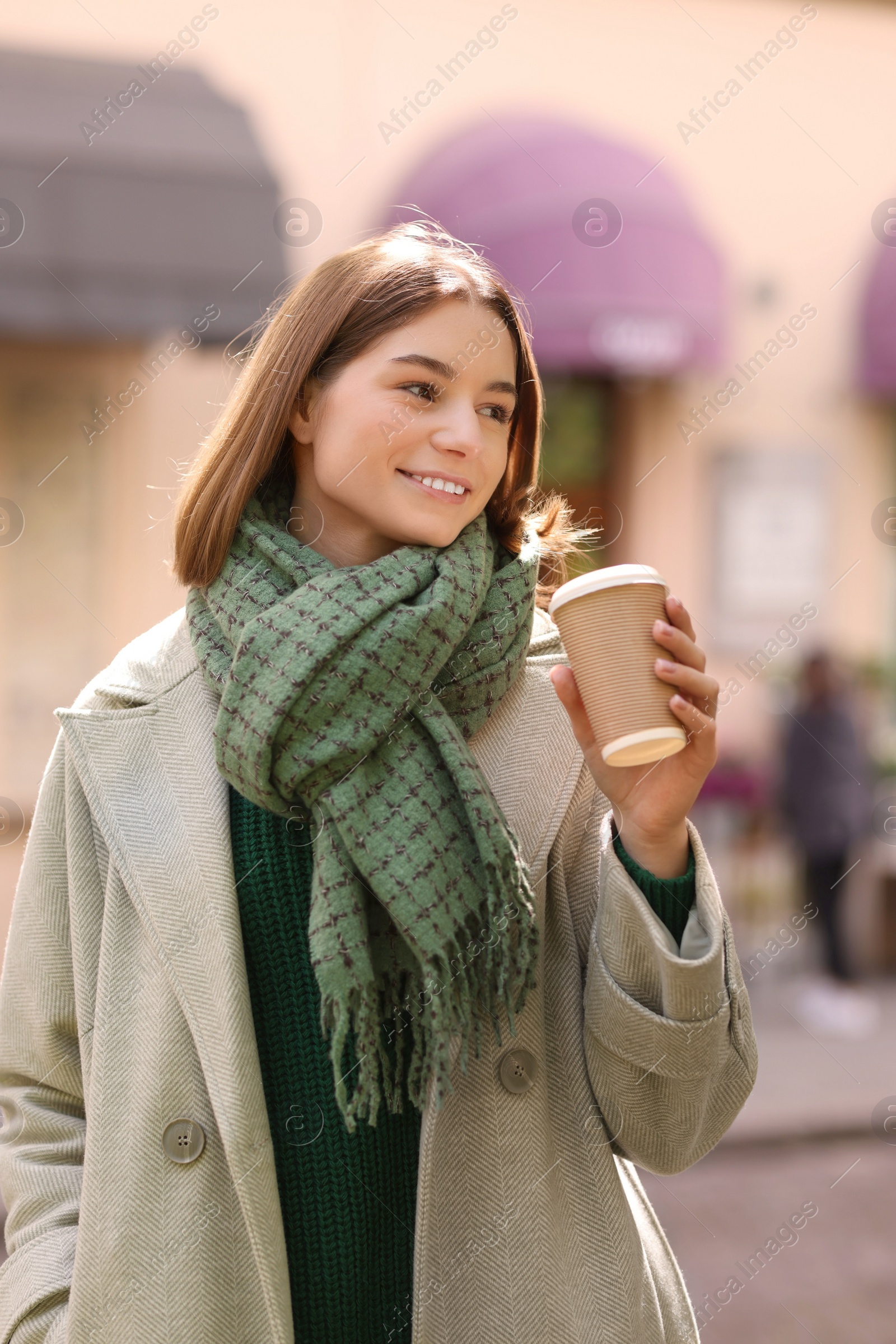 Photo of Beautiful woman in warm scarf with paper cup of coffee on city street