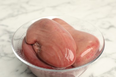 Photo of Bowl with fresh raw pork kidneys on white marble table, closeup