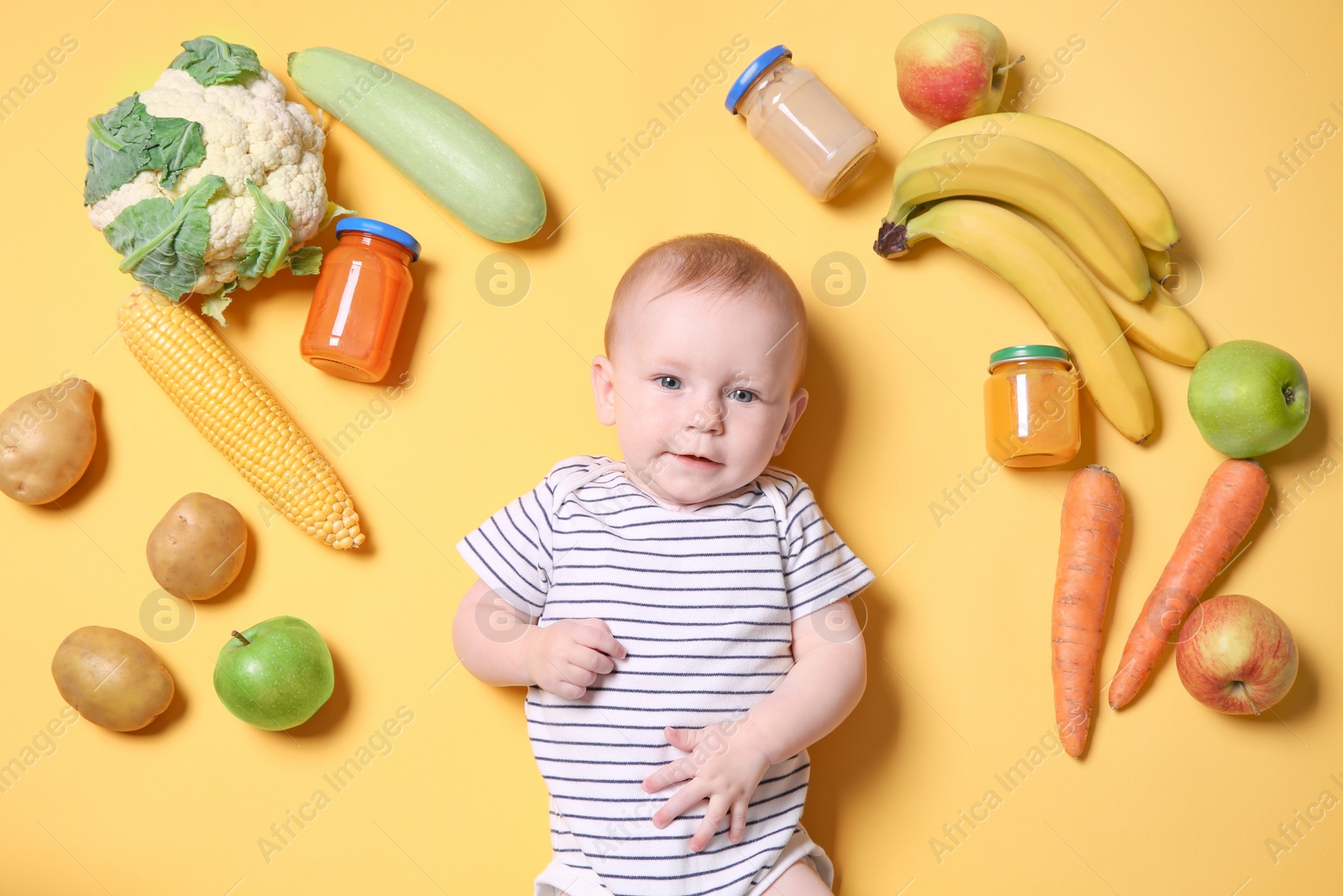 Photo of Cute little child with ingredients and purees in jars on color background, top view. Baby food