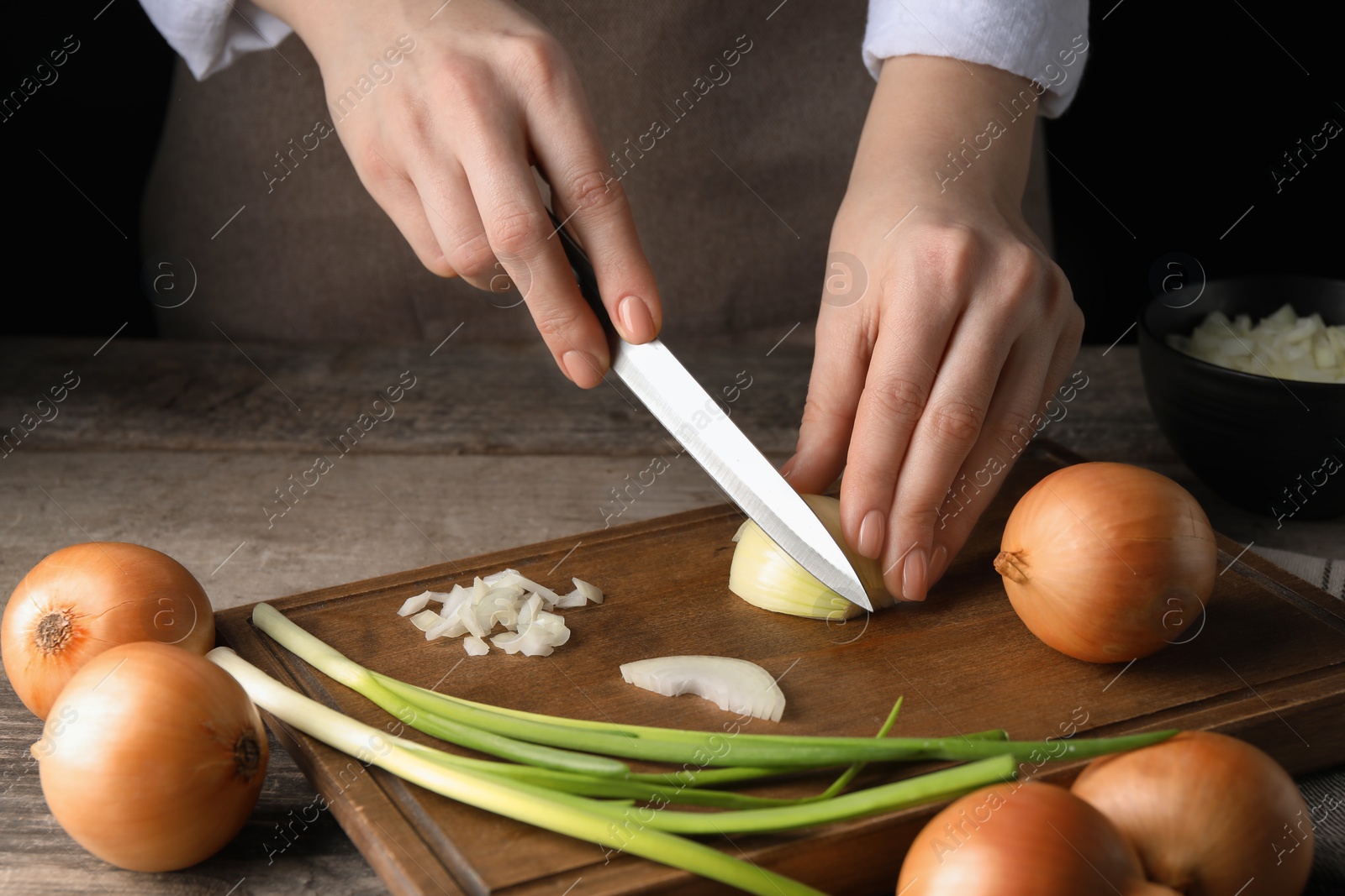 Photo of Woman cutting ripe onion at wooden table, closeup