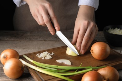 Photo of Woman cutting ripe onion at wooden table, closeup