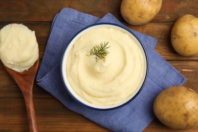 Freshly cooked homemade mashed potatoes, spoon and raw vegetables on wooden table, flat lay