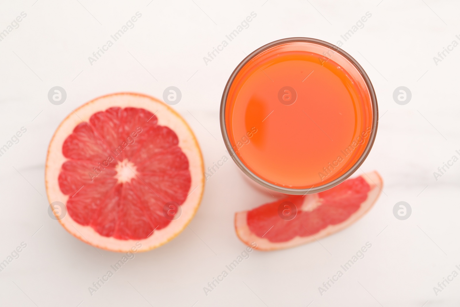 Photo of Tasty grapefruit juice in glass and slices of fresh fruit on white table, top view