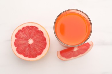 Tasty grapefruit juice in glass and slices of fresh fruit on white table, top view