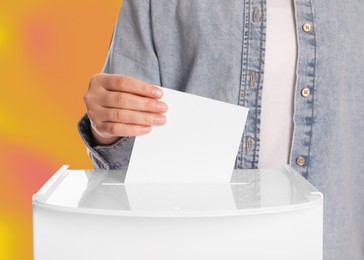 Woman putting her vote into ballot box on color background, closeup
