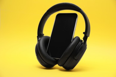 Photo of Modern wireless headphones and smartphone on yellow background