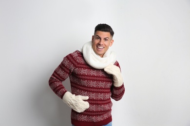 Photo of Handsome man in Christmas sweater, scarf and mittens on white background