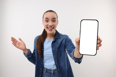 Photo of Surprised young woman showing smartphone in hand on white background, selective focus. Mockup for design