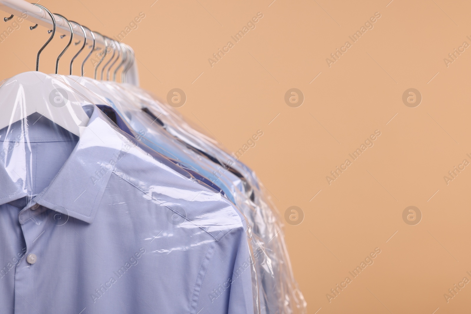 Photo of Dry-cleaning service. Many different clothes in plastic bags hanging on rack against beige background, space for text