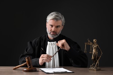 Photo of Judge with gavel and papers sitting at wooden table against black background