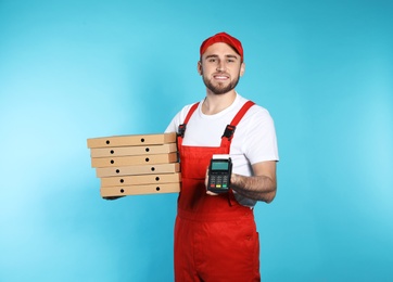 Photo of Smiling courier with pizza boxes and payment terminal on color background