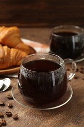 Hot coffee in glass cup and beans on wooden table, closeup