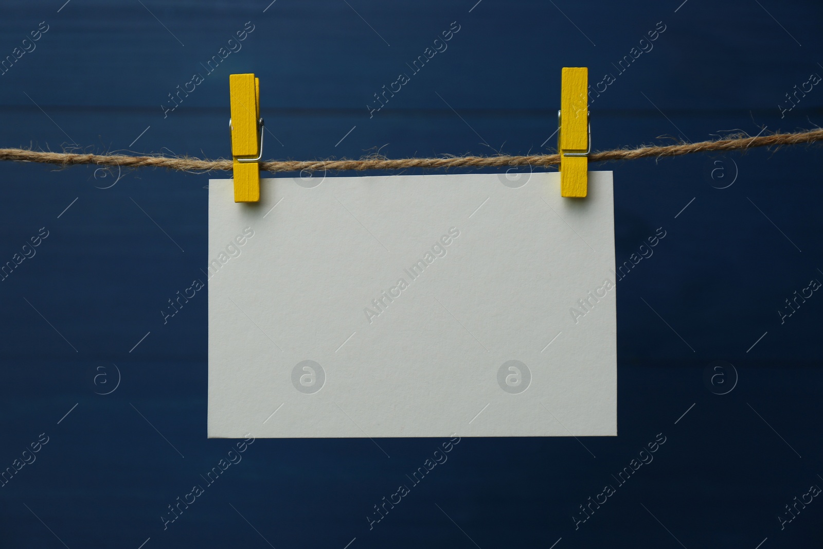 Photo of Clothespins with blank notepaper on twine against blue wooden background. Space for text