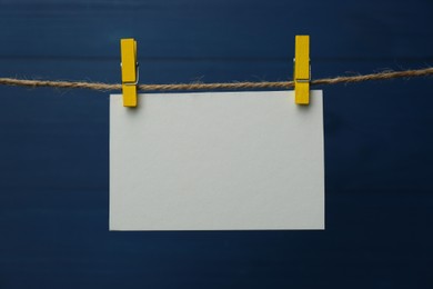Photo of Clothespins with blank notepaper on twine against blue wooden background. Space for text