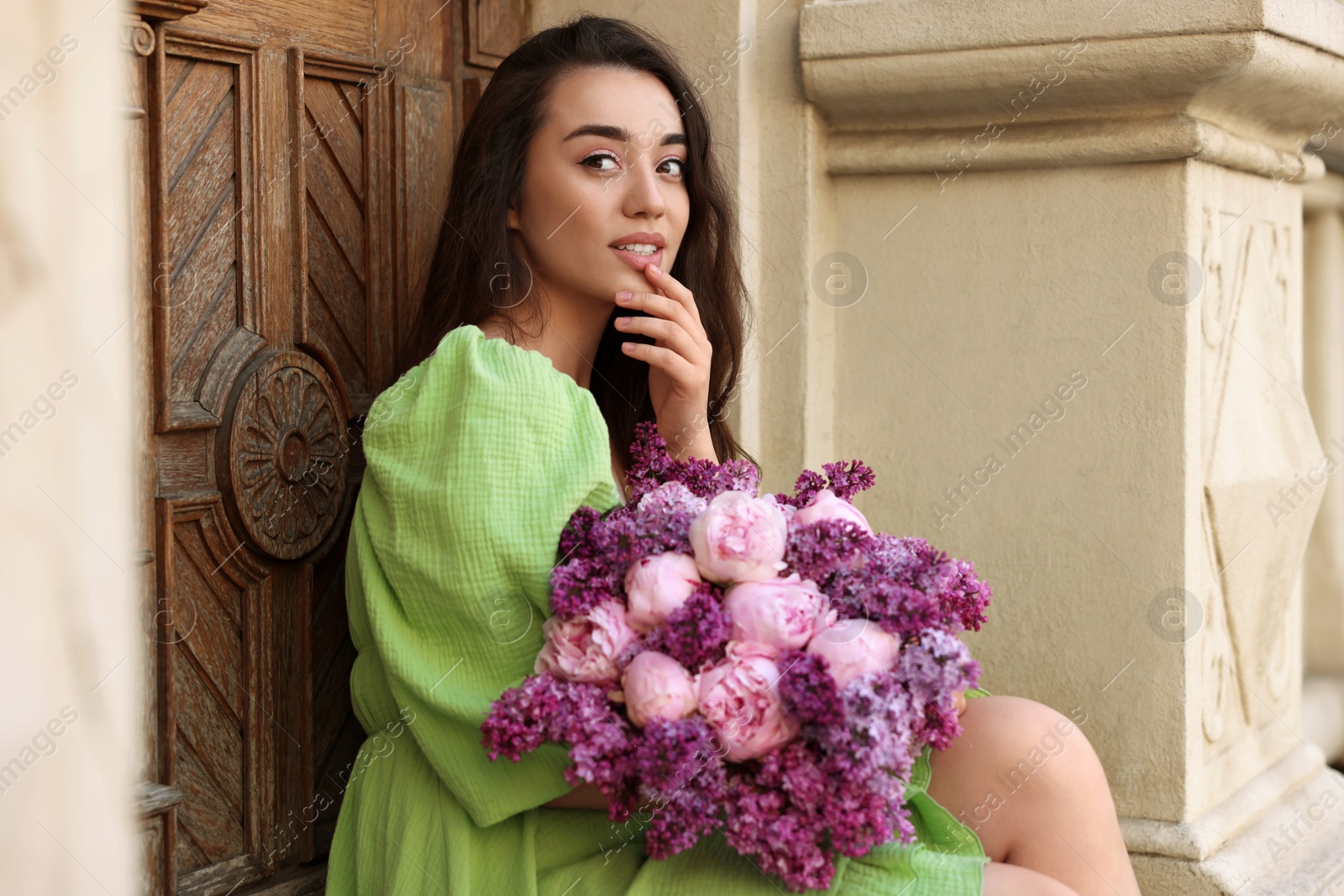 Photo of Beautiful woman with bouquet of spring flowers near building outdoors