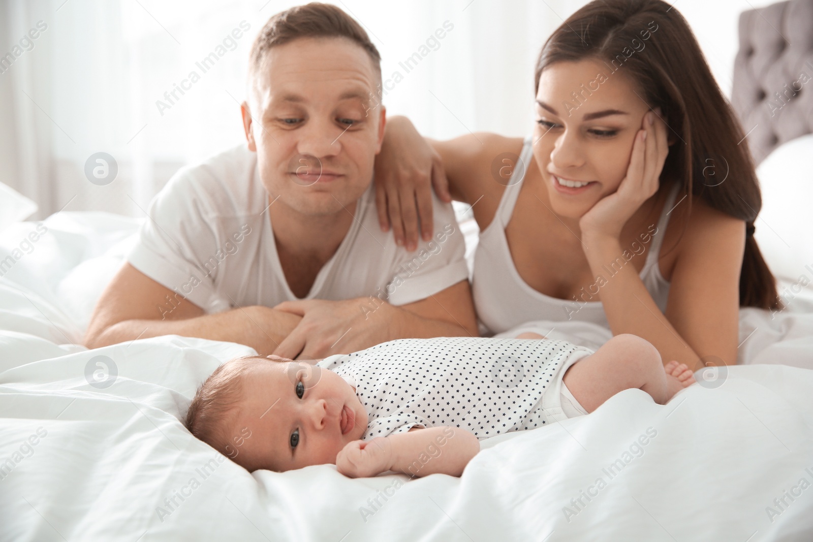 Photo of Happy couple with their newborn baby on bed