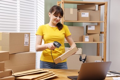 Photo of Parcel packing. Post office worker with scanner reading barcode at wooden table indoors