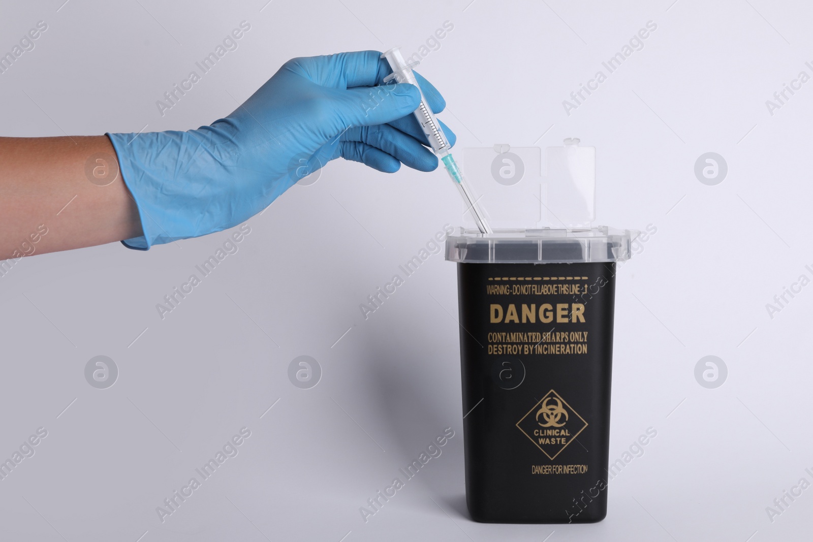 Photo of Doctor throwing used syringe into sharps container on white background, closeup