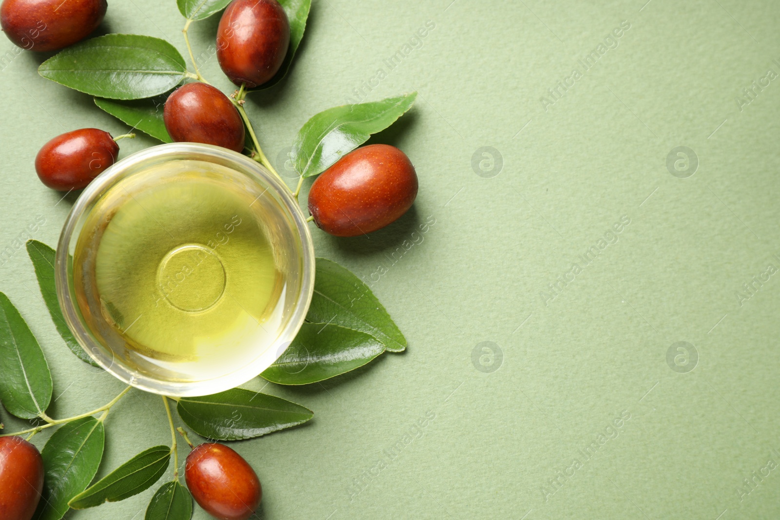 Photo of Glass bowl with jojoba oil and seeds on green background, flat lay. Space for text